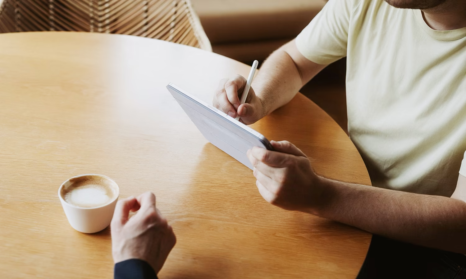 Diskussion am Tisch, die Hände zeigen auf ein Tablet