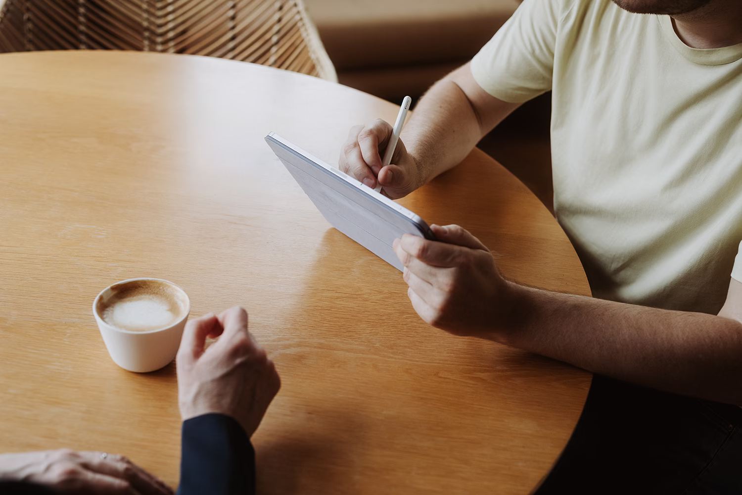 Diskussion am Tisch, die Hände zeigen auf ein Tablet